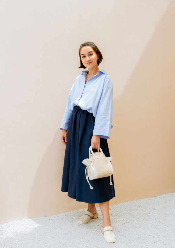 woman with light blue shirt and dark blue skirt holding small bag
